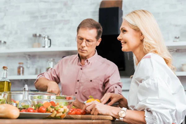 Sorrindo casal adulto preparando salada para jantar juntos na cozinha — Fotografia de Stock