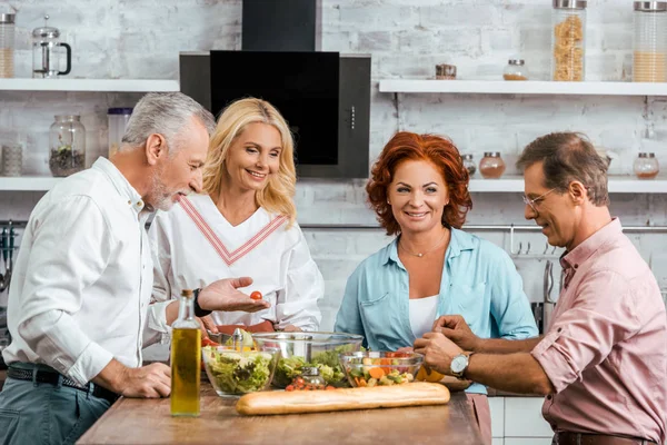 Взрослые старые друзья готовят здоровый салат к ужину дома — стоковое фото