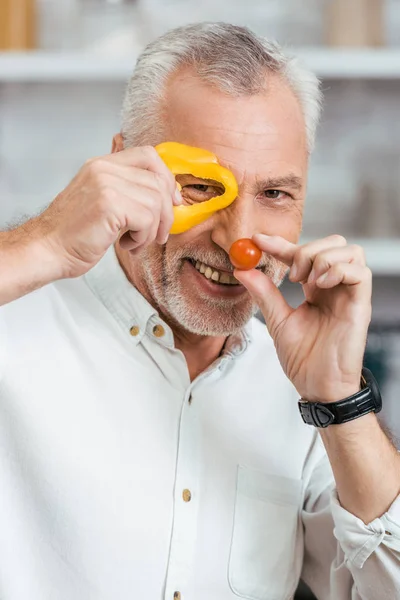 Handsome smiling man having fun with vegetables during preparing salad for dinner at home — Stock Photo