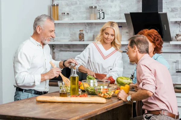 Mature men and women preparing salad for dinner at home — Stock Photo