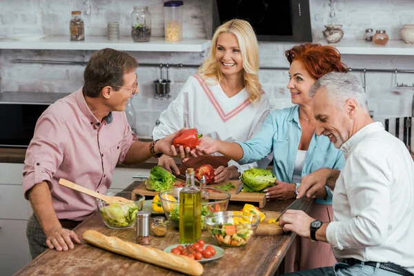 Lächelnde alte Freunde, die Salat für das Abendessen zubereiten und zu Hause reden — Stockfoto