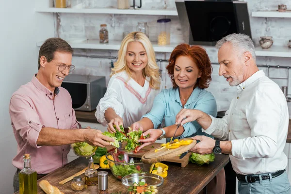 Heureux vieux amis préparer la salade pour le dîner ensemble à la maison et mettre des légumes dans le bol — Photo de stock