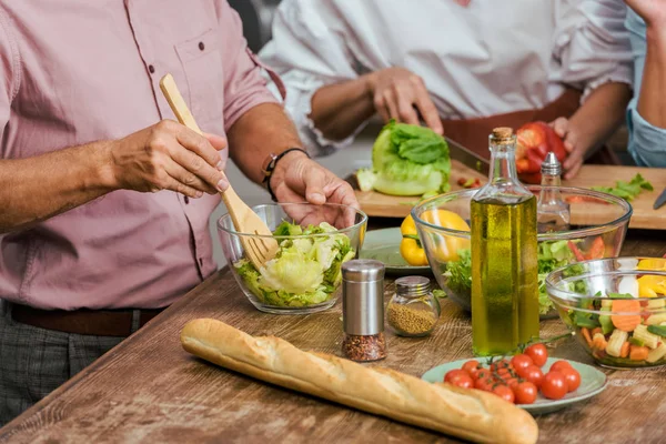 Image recadrée d'amis matures préparant la salade pour le dîner ensemble à la maison — Photo de stock