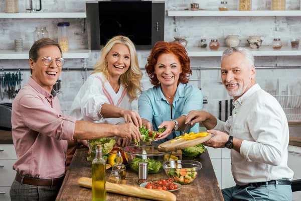 Happy old friends preparing salad for dinner together at home — Stock Photo