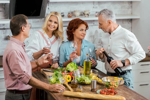 Sorrindo amigos maduros preparando salada para o jantar e comemorando o encontro em casa — Fotografia de Stock