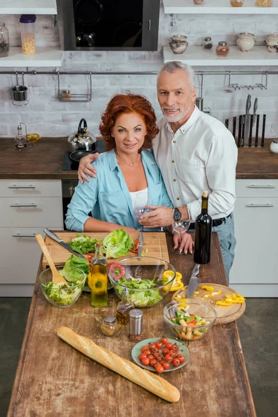 Vista de ángulo alto del marido abrazando esposa durante la preparación de la ensalada para la cena en la cocina — Stock Photo