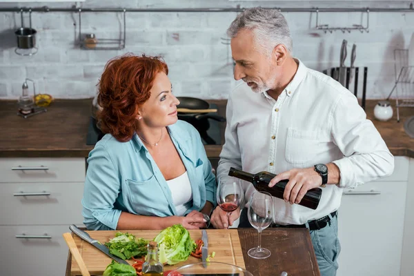 Vista de ángulo alto del marido vertiendo vino a la esposa vidrio durante la preparación de la ensalada para la cena en casa - foto de stock