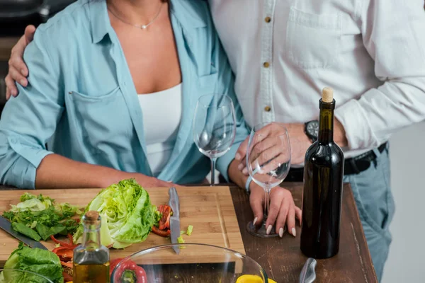Обрізане зображення чоловіка, який обіймає дружину під час приготування салату до вечері на кухні — стокове фото