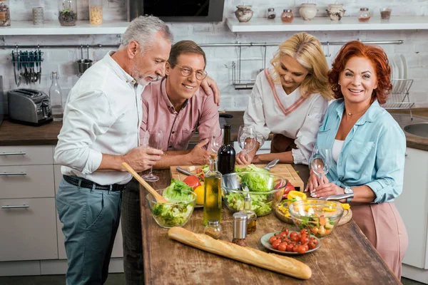 Velhos amigos bebendo vinho, salada orgânica para o jantar na mesa em casa — Fotografia de Stock