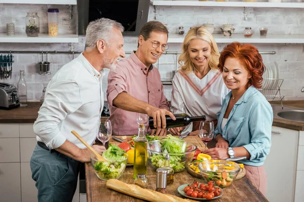 Красивий чоловік поливає вино щасливим старим друзям під час обіду вдома — стокове фото