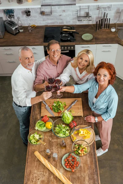 Vista de ángulo alto de viejos amigos sonrientes tintineo con gafas de vino en la cocina - foto de stock