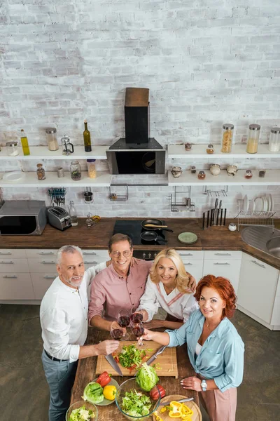 Vista de alto ângulo de velhos amigos clinking com vinhedos na cozinha e olhando para a câmera — Fotografia de Stock