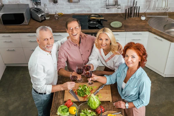 Vista de ángulo alto de viejos amigos felices tintineo con gafas de vino en la cocina - foto de stock