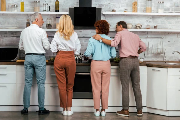 Vista posteriore di due coppie mature che cucinano insieme in cucina — Foto stock