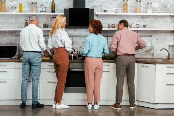 Vista posterior de amigos maduros hombres y mujeres cocinando juntos en la cocina - foto de stock