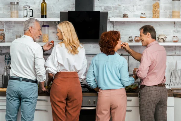 Back view of men feeding mature women while standing together in kitchen — Stock Photo