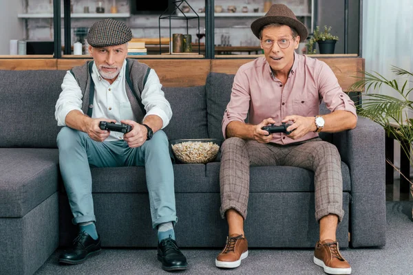 Schöne reife Männer, die Steuerknüppel benutzen und in die Kamera schauen, während sie zusammen auf der Couch sitzen — Stockfoto