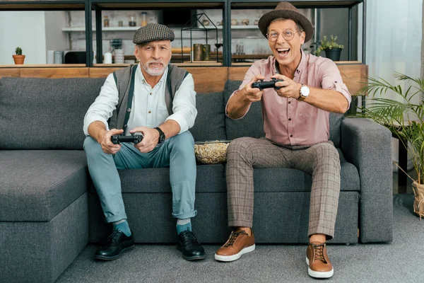 Handsome mature men sitting on sofa and playing with joysticks — Stock Photo
