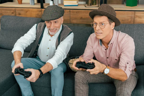 Dos amigos varones maduros jugando con joysticks en casa - foto de stock