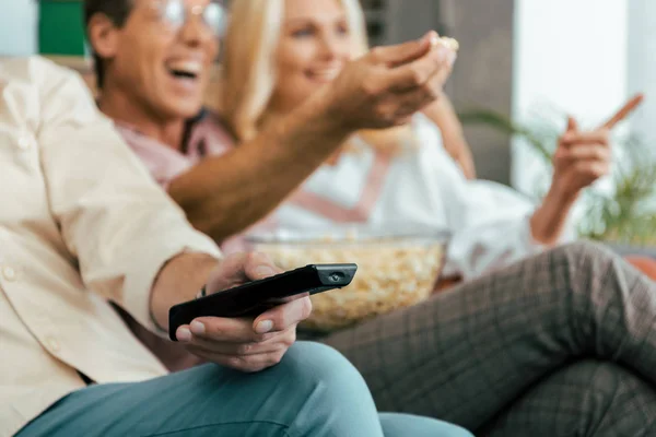 Ritagliato colpo di amici maturi utilizzando telecomando e mangiare popcorn mentre si guarda la tv insieme — Foto stock