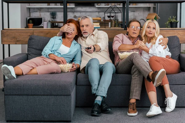 Casais maduros assustados sentados no sofá e assistindo tv juntos — Fotografia de Stock