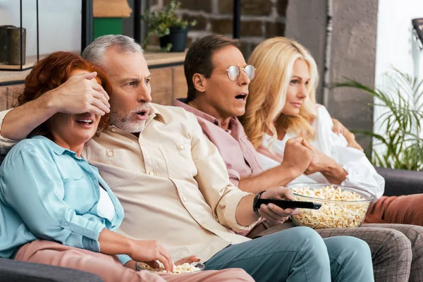 Перепуганные взрослые друзья сидят на диване и смотрят телевизор вместе — стоковое фото