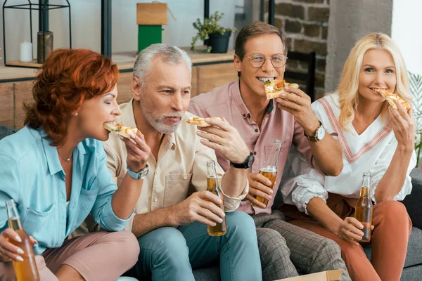 Dois casais maduros bebendo cerveja e comendo pizza juntos em casa — Fotografia de Stock