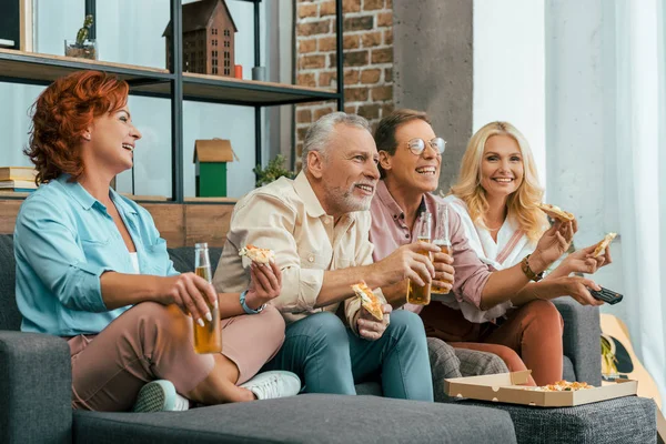 Velhos amigos sorridentes comendo pizza e bebendo cerveja juntos em casa — Fotografia de Stock