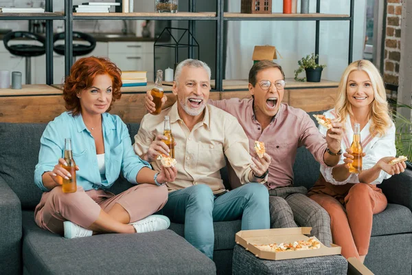 Viejos amigos felices bebiendo cerveza y comiendo pizza en casa - foto de stock