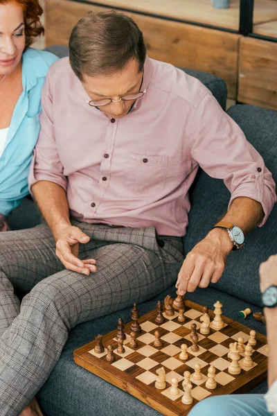 Vista de ángulo alto de hombre maduro en anteojos jugando ajedrez con amigos en casa - foto de stock