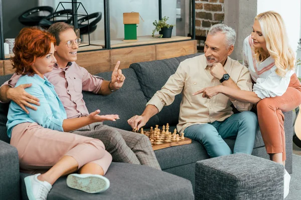 Amigos maduros felices reuniéndose y jugando al ajedrez en casa - foto de stock