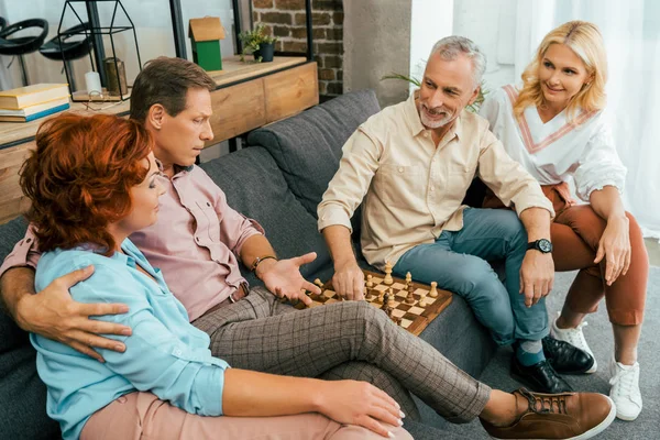 Two mature couples sitting on couch and playing chess at home — Stock Photo