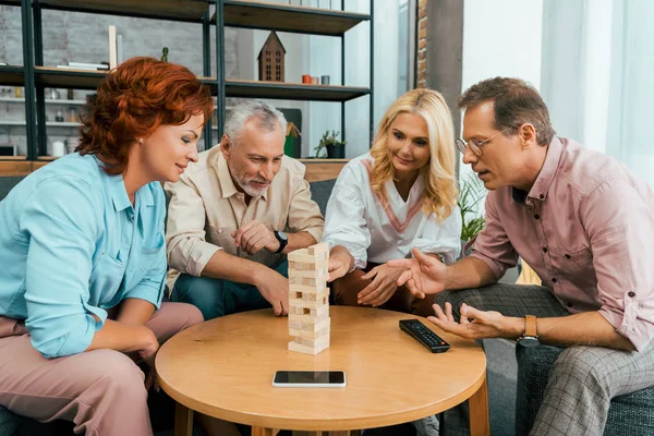 Two mature couples spending time together and playing with wooden blocks at home — Stock Photo