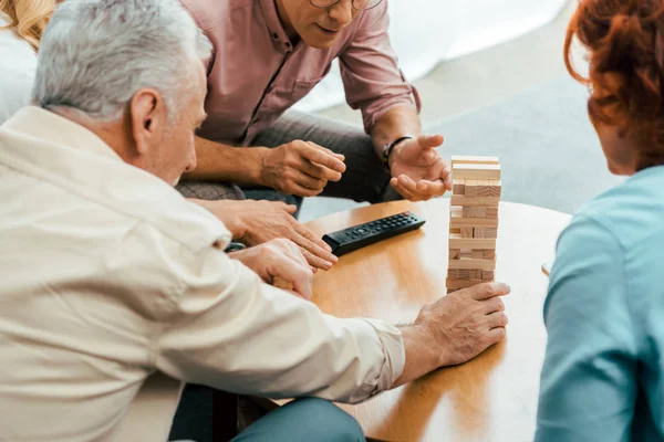 Обрезанный снимок зрелых друзей, играющих с деревянными блоками на столе дома — стоковое фото