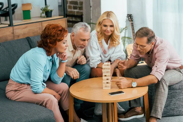 Amigos maduros enfocados jugando con bloques de madera en casa - foto de stock