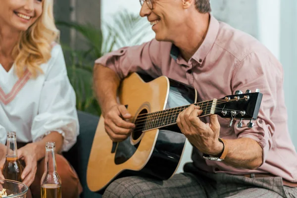 Cortado tiro de homem maduro tocando guitarra e olhando para bela mulher sorridente em casa — Fotografia de Stock