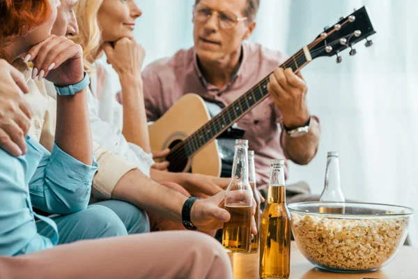 Cropped shot of old friends drinking beer and playing acoustic guitar at home — Stock Photo