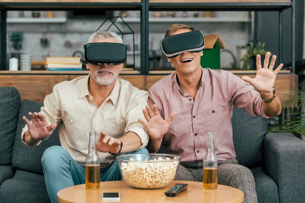 Счастливые зрелые мужчины сидят на диване и используют гарнитуры виртуальной реальности — стоковое фото