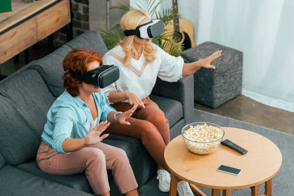 Vue grand angle des amies matures utilisant des casques de réalité virtuelle à la maison — Photo de stock