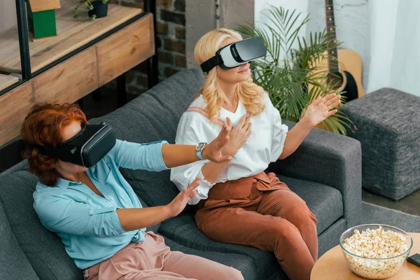 Высокий угол обзора зрелых женщин, сидящих на диване и использующих гарнитуры виртуальной реальности — стоковое фото