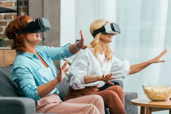 Femmes mûres heureuses assises sur le canapé et utilisant des casques de réalité virtuelle — Photo de stock