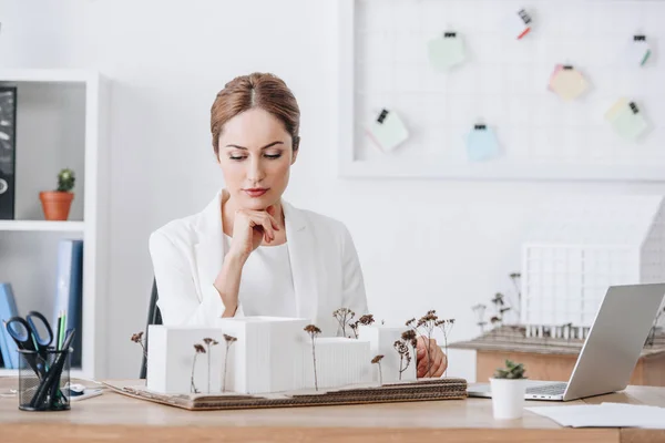 Pensativo mujer arquitecto mirando casa modelo en oficina - foto de stock