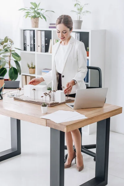 Привлекательная женщина-архитектор работает с моделью дома в офисе — стоковое фото
