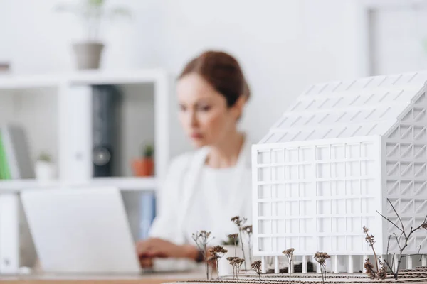 Foco seletivo de modelo de casa e arquiteto que trabalha com computador portátil no escritório — Fotografia de Stock