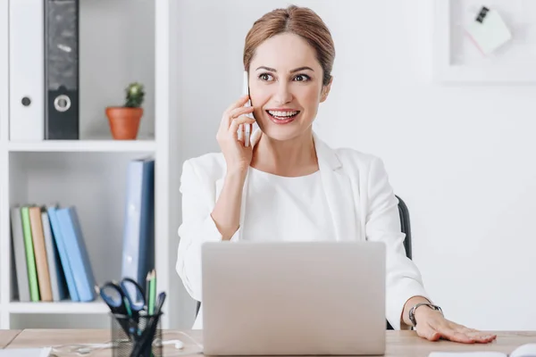 Erfolgreiche Geschäftsfrau spricht am Arbeitsplatz mit Smartphone und Laptop — Stockfoto