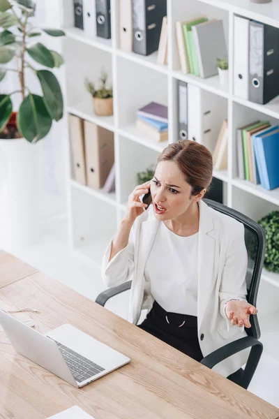 Bella donna d'affari stressata che parla sullo smartphone in ufficio con il computer portatile — Foto stock