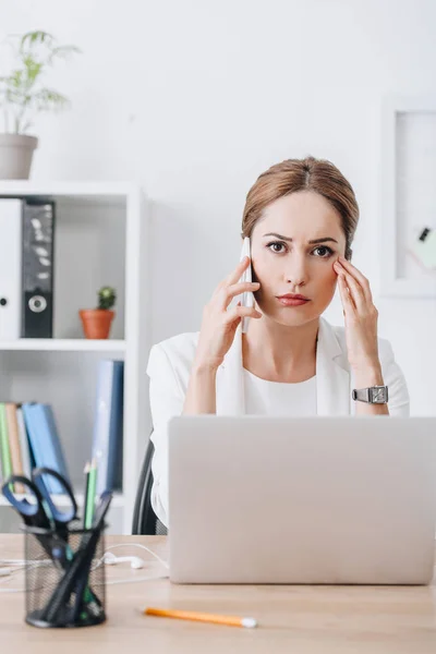 Worried businesswoman with smartphone and laptop at workplace — Stock Photo