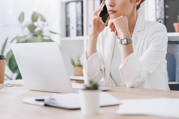 Cropped view of frustrated businesswoman working with smartphone and laptop at workplace — Stock Photo