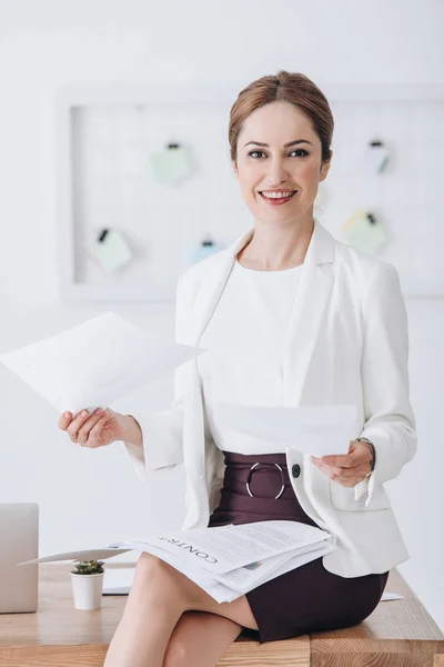 Hermosa mujer de negocios sonriente haciendo papeleo sentado en la mesa con el ordenador portátil - foto de stock