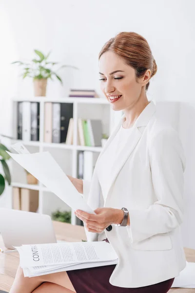 Attraktive Geschäftsfrau, die Papierkram erledigt, sitzt im Büro auf dem Tisch — Stockfoto